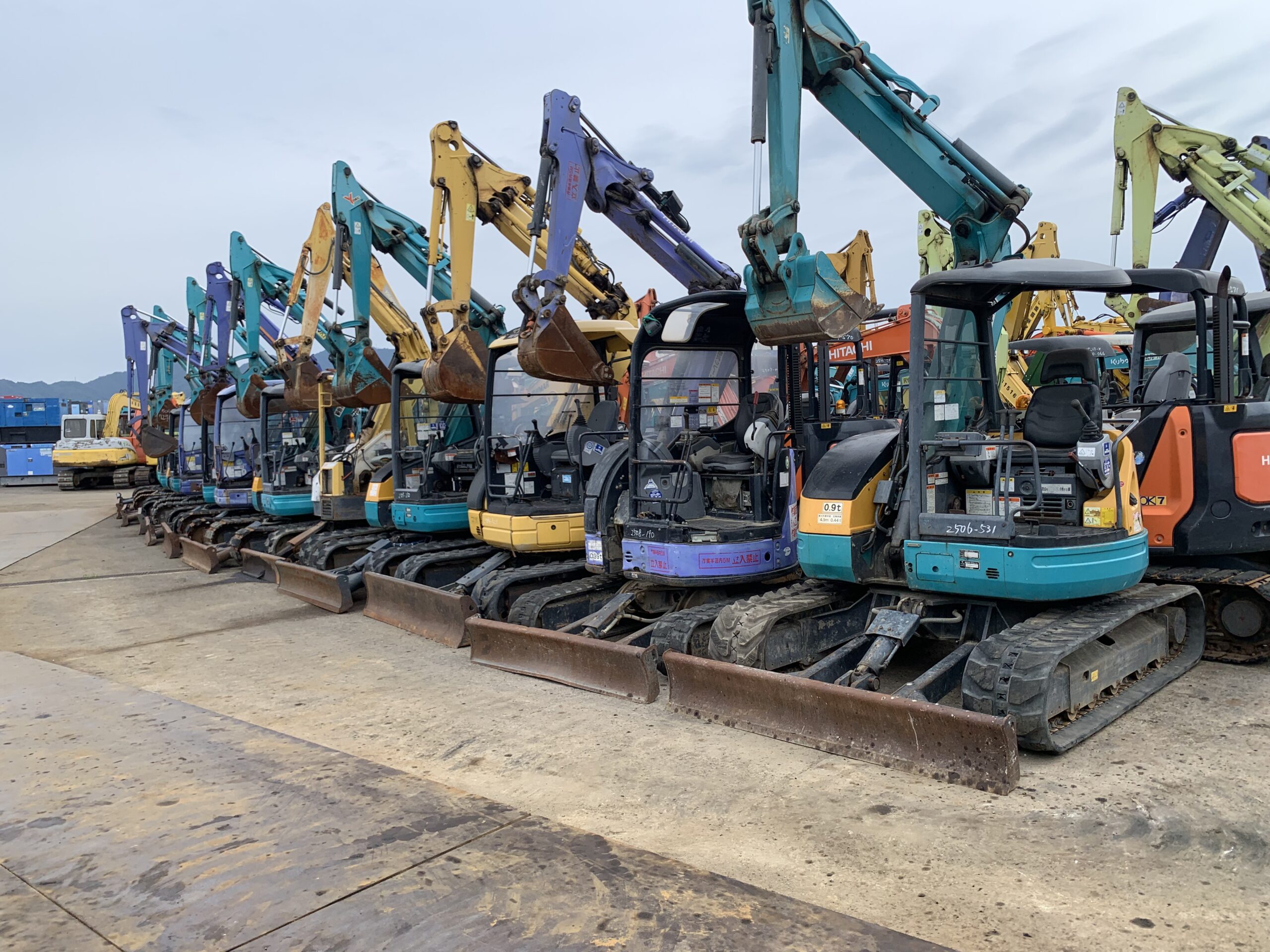 Row of used Japanese mini excavators lined up in an export yard
